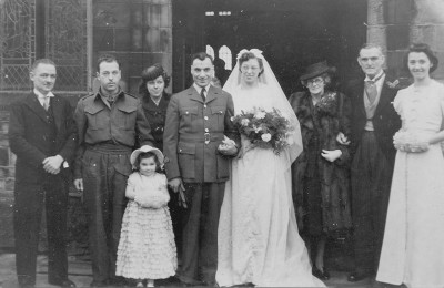 In the wedding group are: Andrew Ross, my brother-in-law, Paul Barrett, who had managed his leave to be best man. (Brother Bill, unfortunately, couldn’t make it.) Next is my sister Ethel, standing behind her elder daughter, Judith Ann. On the other side is mother, father, and Peggy Hall, one of my best friends. My dress was ivory satin brocade, with a bouquet of orchids and white carnations. Judith’s dress was blue taffeta, and Peggy’s ivory taffeta, trimmed with the blue. The head-dresses and muffs were made to match.